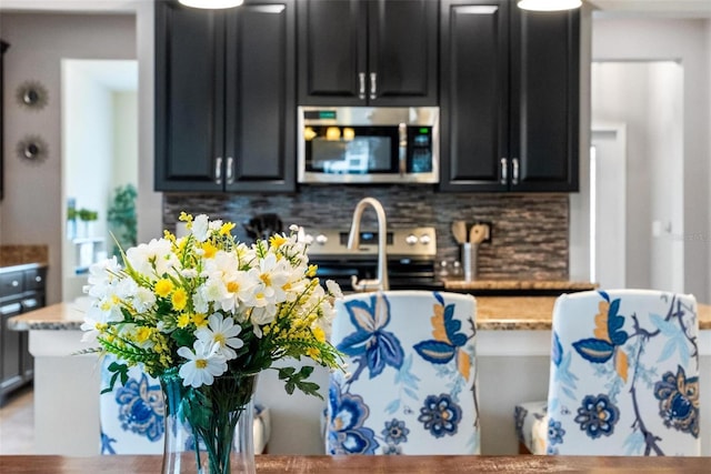 kitchen featuring stainless steel appliances, dark cabinets, tasteful backsplash, and light stone countertops