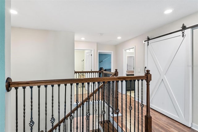 hall featuring an upstairs landing, wood finished floors, recessed lighting, baseboards, and a barn door