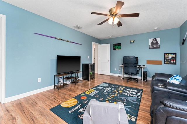 living area featuring wood finished floors, a ceiling fan, baseboards, a desk, and a textured ceiling