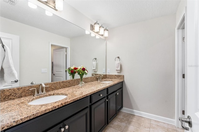 bathroom featuring baseboards, double vanity, tile patterned flooring, and a textured ceiling