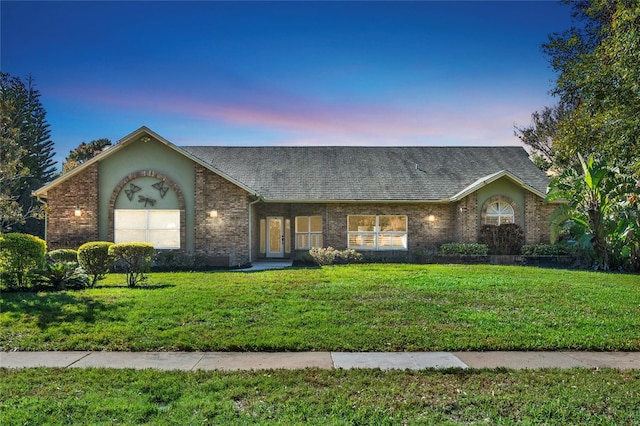 ranch-style house with a yard, a shingled roof, and brick siding