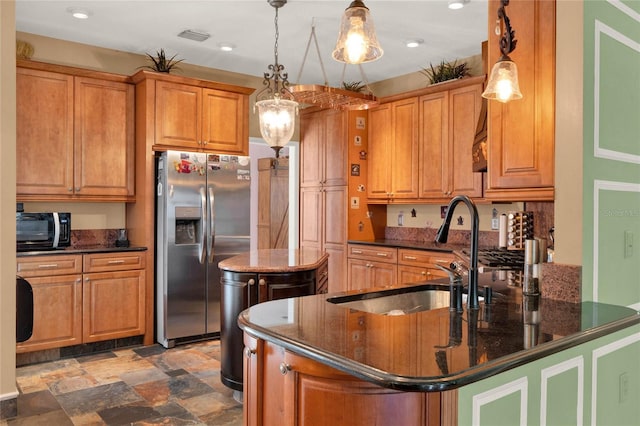 kitchen featuring brown cabinetry, stainless steel fridge with ice dispenser, dark stone countertops, black microwave, and a sink