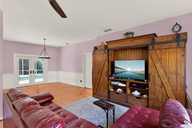 living room featuring wood finished floors, french doors, a wainscoted wall, and a barn door