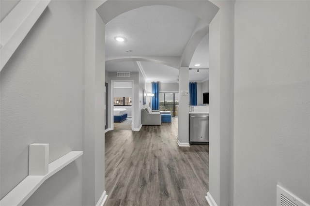 hallway featuring baseboards, visible vents, arched walkways, and wood finished floors