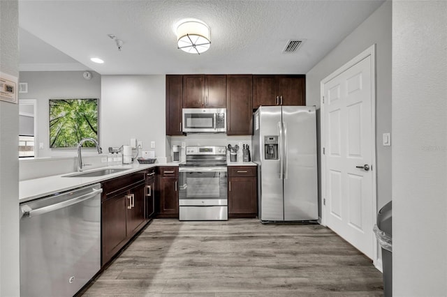 kitchen featuring stainless steel appliances, light countertops, light wood-style floors, a sink, and dark brown cabinetry