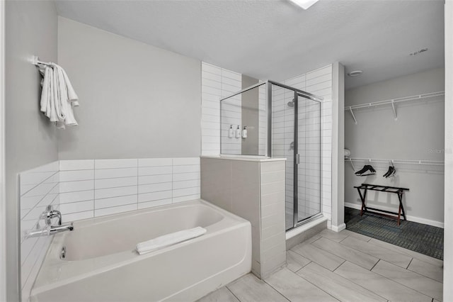 full bathroom with a textured ceiling, a stall shower, a walk in closet, and a bath