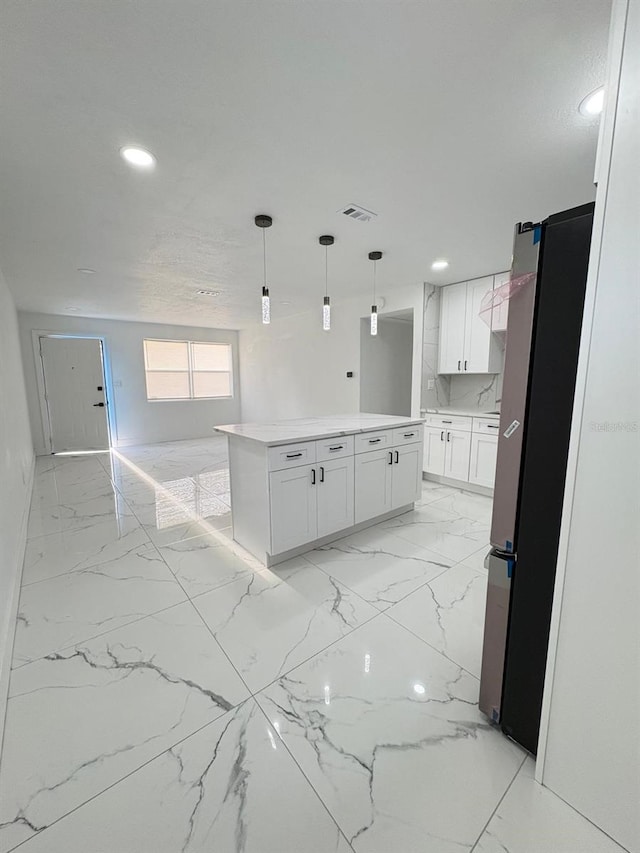 kitchen featuring light countertops, visible vents, freestanding refrigerator, white cabinets, and a kitchen island