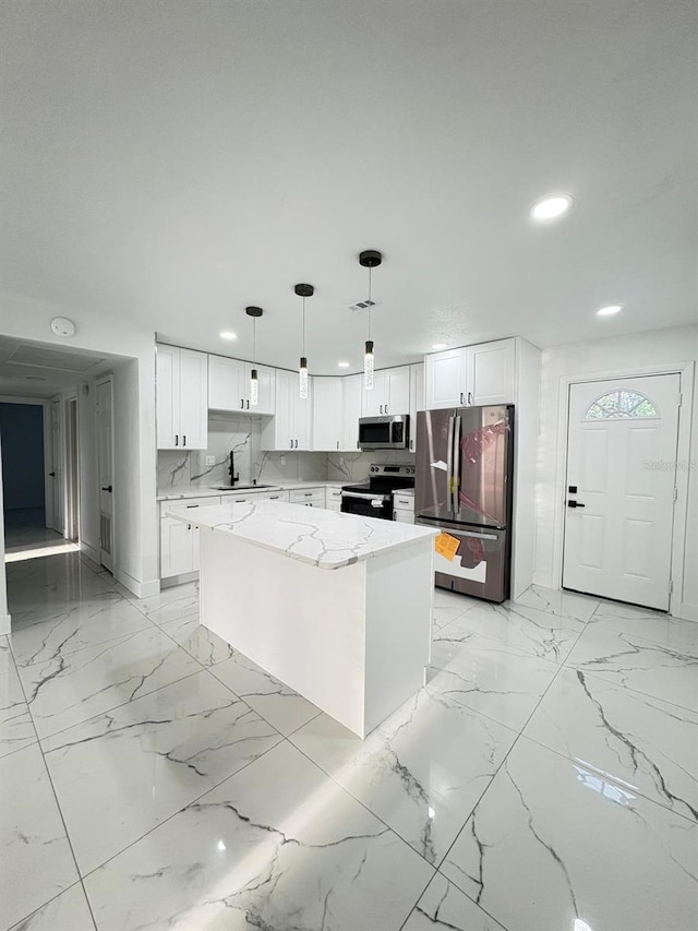 kitchen with appliances with stainless steel finishes, white cabinetry, a kitchen island, and light stone countertops