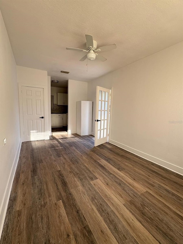 unfurnished living room with a textured ceiling, ceiling fan, visible vents, baseboards, and dark wood finished floors