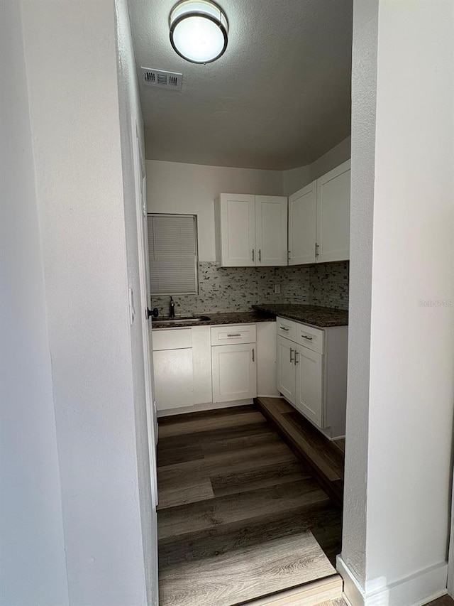 kitchen with dark countertops, white cabinets, a sink, and visible vents