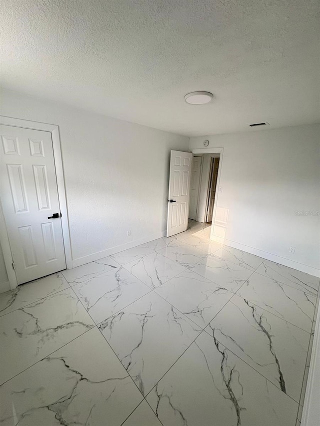 unfurnished room featuring marble finish floor, baseboards, and a textured ceiling