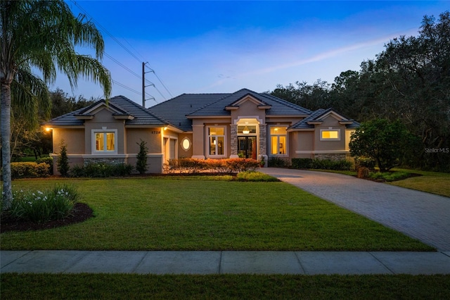 prairie-style home featuring decorative driveway, a tile roof, stucco siding, a lawn, and stone siding