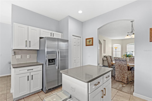 kitchen featuring arched walkways, stainless steel refrigerator with ice dispenser, tasteful backsplash, white cabinetry, and a kitchen island