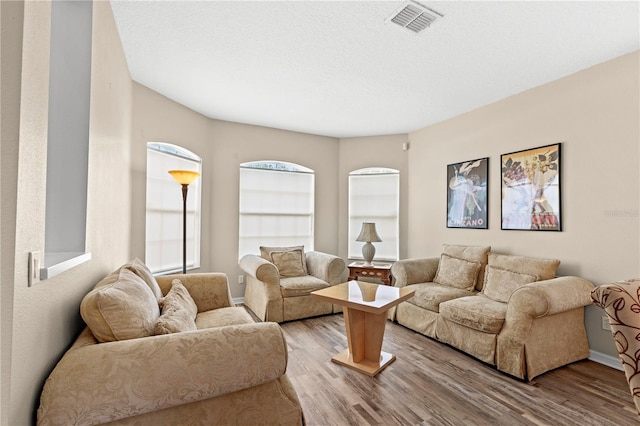 living room featuring visible vents, light wood-style flooring, and a textured ceiling