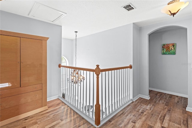 corridor featuring arched walkways, light wood-style flooring, visible vents, baseboards, and an inviting chandelier