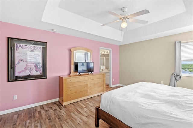 bedroom featuring a raised ceiling, light wood-style flooring, baseboards, and a textured ceiling