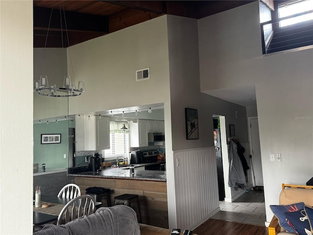 kitchen featuring visible vents, a wainscoted wall, electric stove, a sink, and a towering ceiling