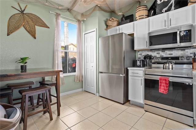 kitchen featuring light tile patterned floors, stainless steel appliances, baseboards, white cabinets, and tasteful backsplash