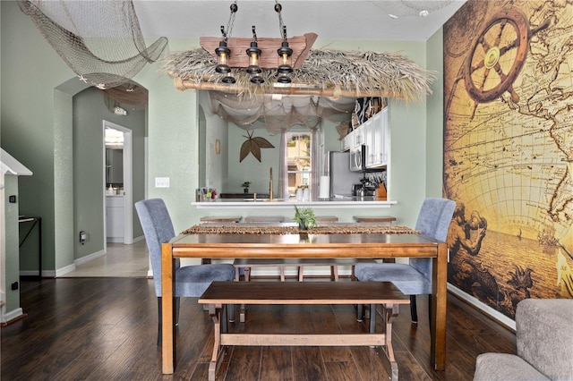 dining room with baseboards, arched walkways, and wood finished floors