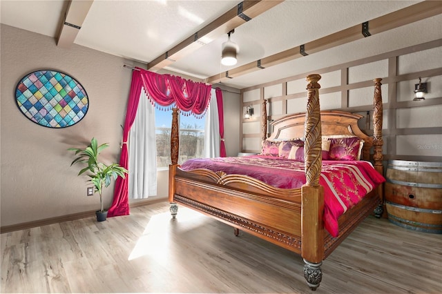 bedroom with beamed ceiling, baseboards, and wood finished floors