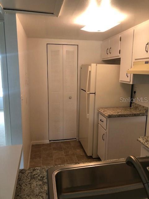 kitchen with under cabinet range hood, a sink, white cabinets, freestanding refrigerator, and dark stone counters