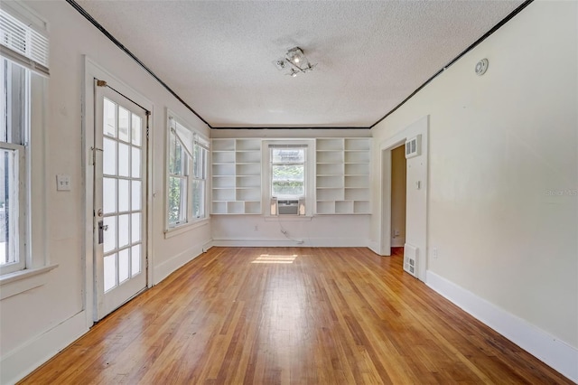 spare room featuring built in features, baseboards, visible vents, light wood-style flooring, and a textured ceiling