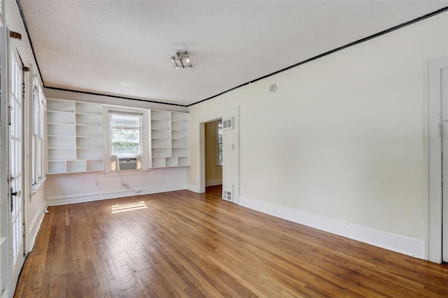 empty room featuring visible vents, baseboards, wood-type flooring, cooling unit, and a textured ceiling