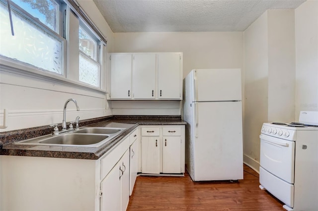 kitchen with dark wood-style floors, dark countertops, white cabinetry, a sink, and white appliances