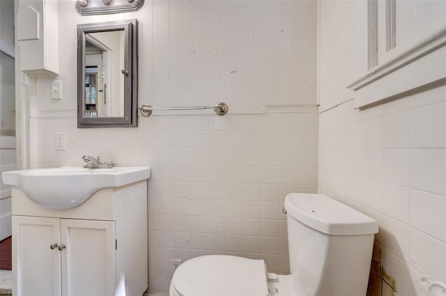 bathroom with toilet, tile walls, and vanity