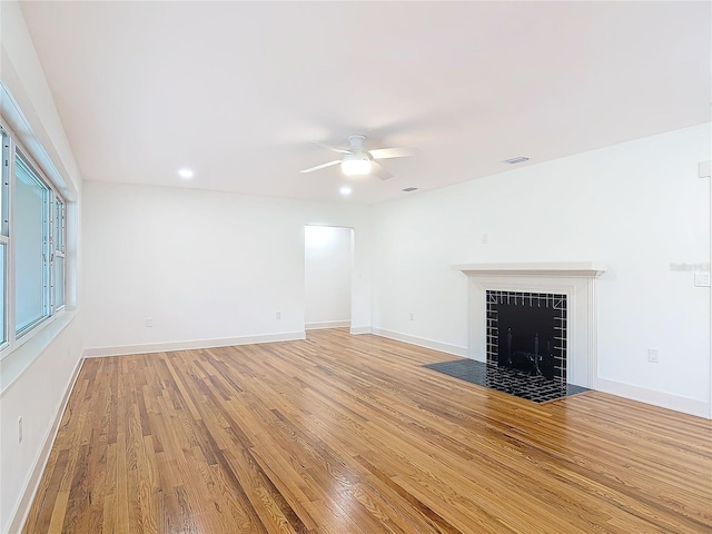 unfurnished living room featuring light wood-style flooring, a fireplace, visible vents, a ceiling fan, and baseboards