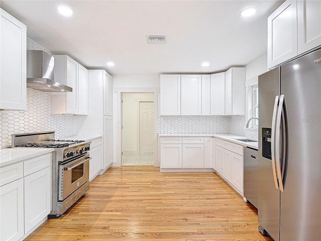 kitchen featuring stainless steel appliances, visible vents, light wood-style flooring, a sink, and wall chimney exhaust hood