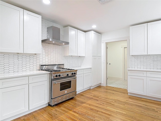 kitchen with white cabinets, wall chimney range hood, high end stainless steel range oven, light countertops, and light wood-style floors