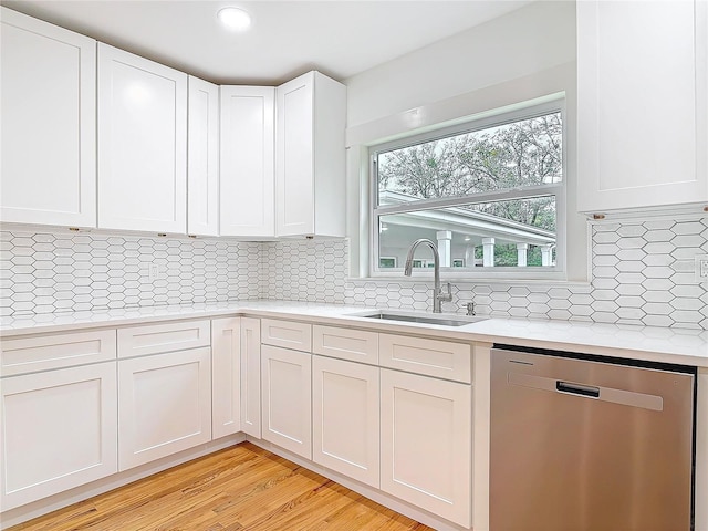 kitchen with light countertops, decorative backsplash, stainless steel dishwasher, white cabinets, and a sink