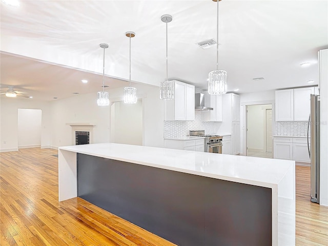 kitchen featuring stainless steel appliances, white cabinets, light wood-style flooring, and wall chimney range hood