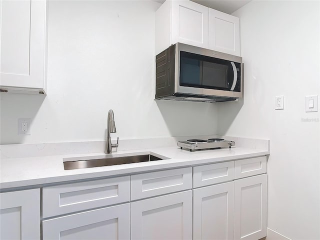 kitchen featuring light countertops, stainless steel microwave, a sink, and white cabinetry