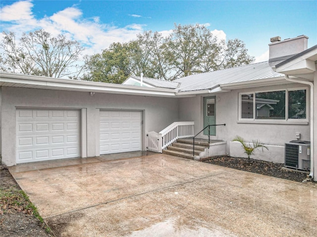 ranch-style house with a garage, concrete driveway, metal roof, central air condition unit, and stucco siding