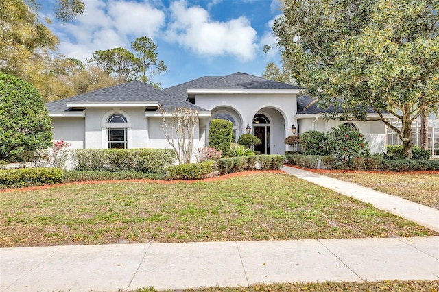 ranch-style home with a shingled roof, a front yard, and stucco siding