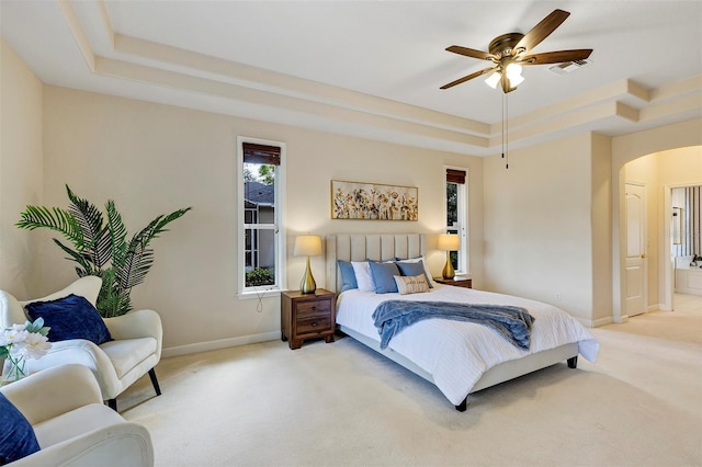 bedroom with arched walkways, a tray ceiling, visible vents, and light colored carpet