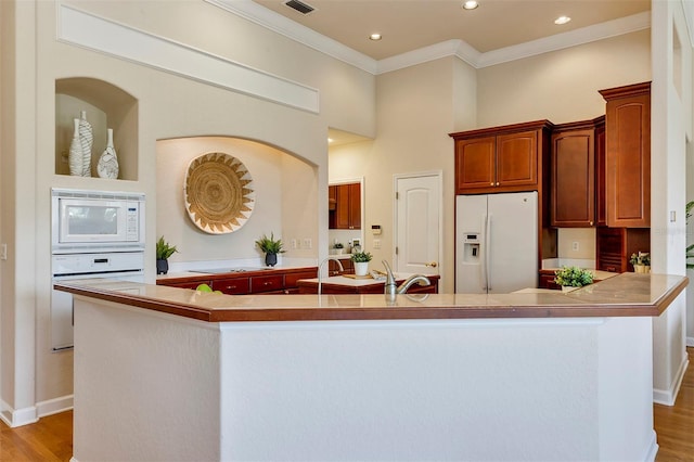 kitchen featuring crown molding, a large island, a towering ceiling, light wood-type flooring, and white appliances