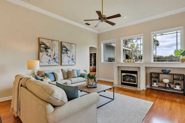 living room with baseboards, arched walkways, ornamental molding, wood finished floors, and a fireplace