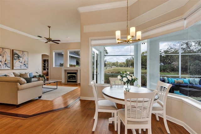 dining room featuring wood finished floors, ornamental molding, arched walkways, and a glass covered fireplace