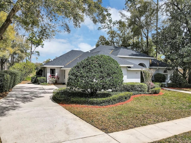 single story home with concrete driveway, roof with shingles, a front yard, and stucco siding