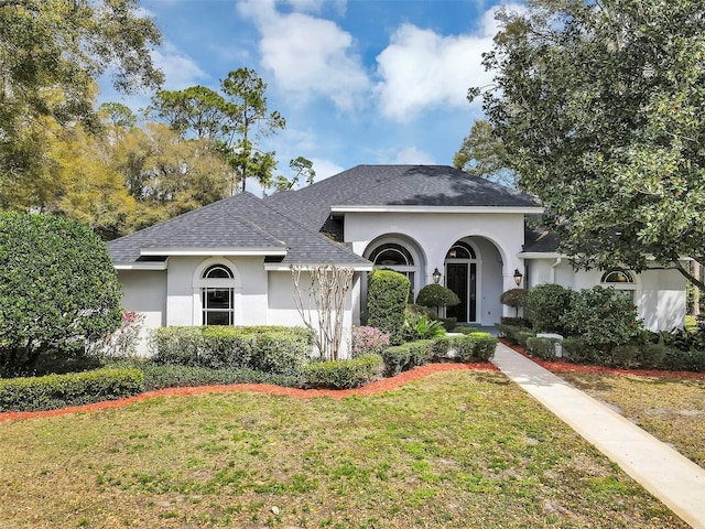 view of front of home featuring a shingled roof, a front yard, and stucco siding