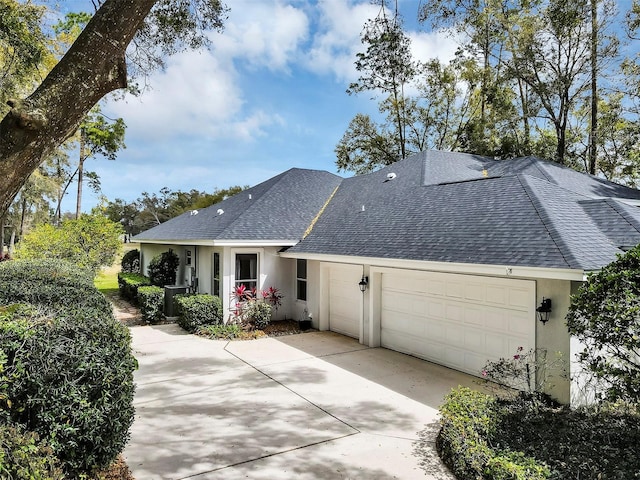 view of front facade featuring a garage, concrete driveway, roof with shingles, and stucco siding