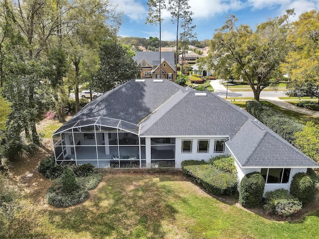 back of house featuring a shingled roof, a lanai, and a lawn