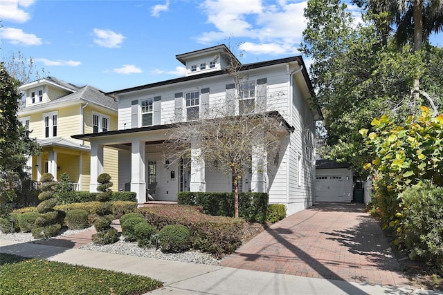 traditional style home with a garage, a porch, decorative driveway, and an outbuilding