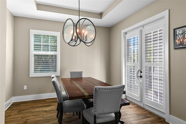 dining space with a tray ceiling, dark wood finished floors, baseboards, and an inviting chandelier