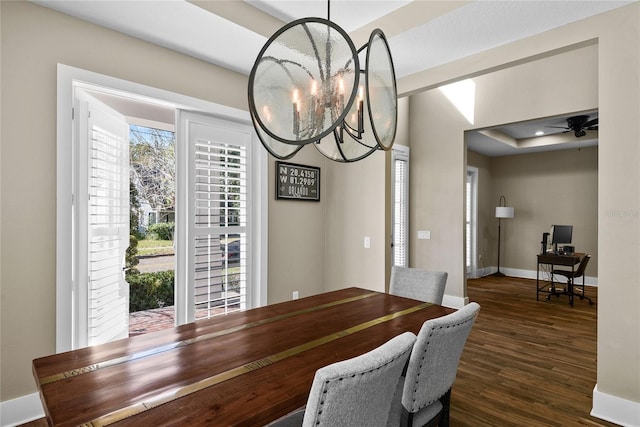 dining room with a tray ceiling, baseboards, wood finished floors, and ceiling fan with notable chandelier