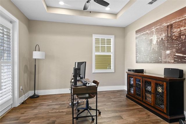 office space with baseboards, visible vents, ceiling fan, wood finished floors, and a tray ceiling