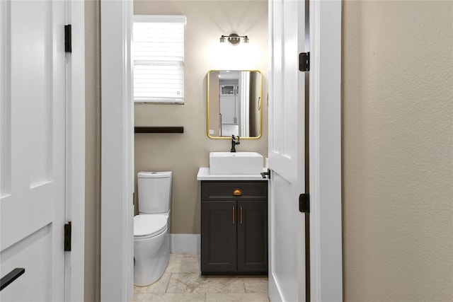 half bathroom featuring marble finish floor, baseboards, vanity, and toilet